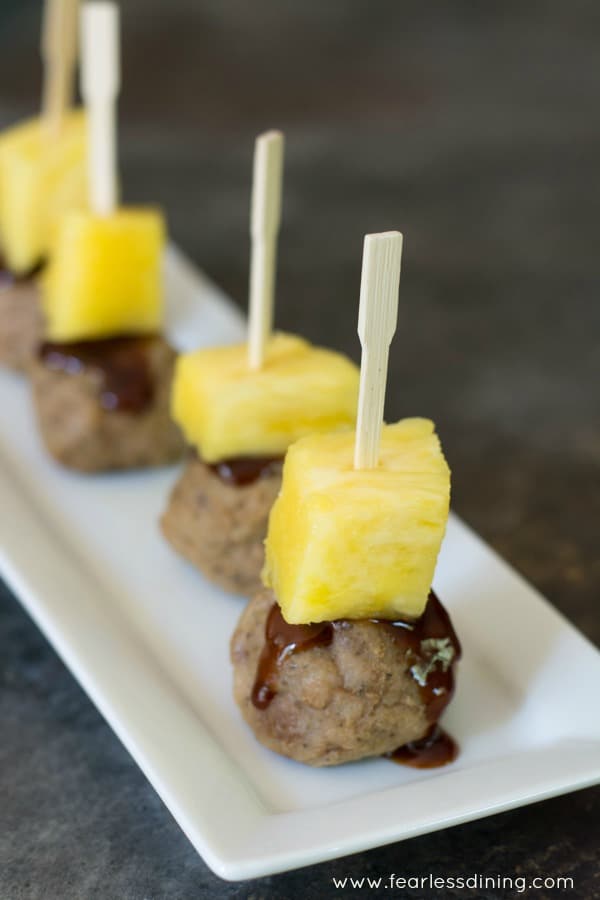Meatballs with pineapple and barbecue sauce. A toothpick is holding them together on a plate.