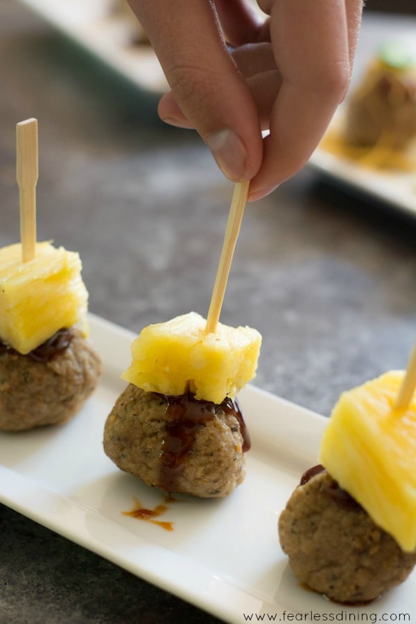 A hand grabbing a toothpick with a meatball and pineapple chunk.