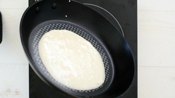 Tilting a pan to spread the crepes batter.