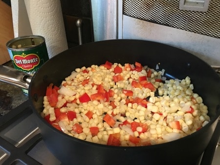 Corn, red pepper and onion cooking in a pan on the stove.