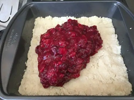 Adding the cranberry sauce layer on top of the shortbread layer