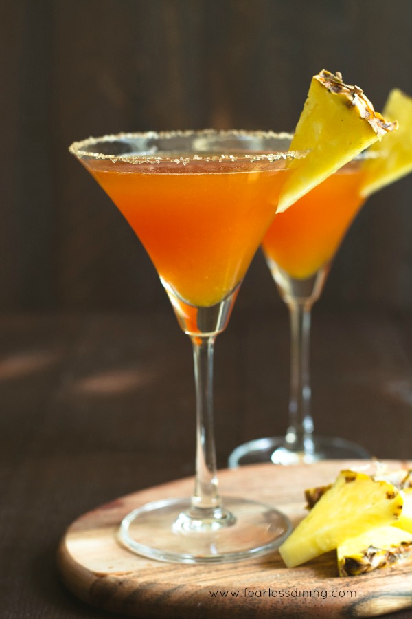 Two prickly pear margaritas on a cutting board. There are slices of pineapple on the cutting board, and garnishing each glass.