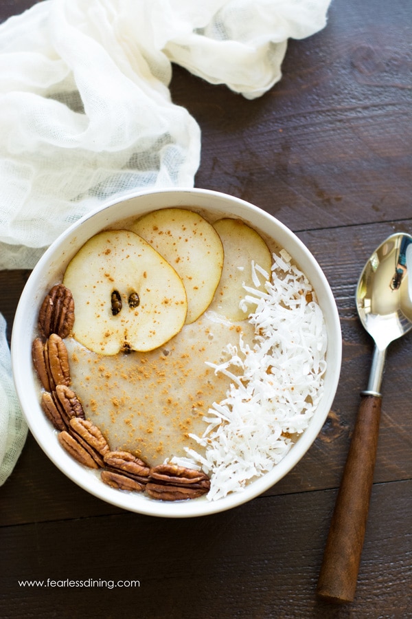 Top view of a pear smoothie bowl. There are sliced pears, pecans and coconut. A wooden handled spoon is next to the bowl.