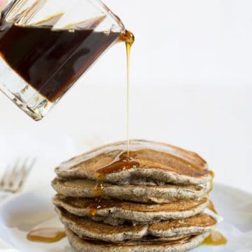 Pouring syrup over a stack of buckwheat pancakes.