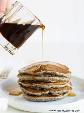 Pouring syrup over a stack of buckwheat pancakes.