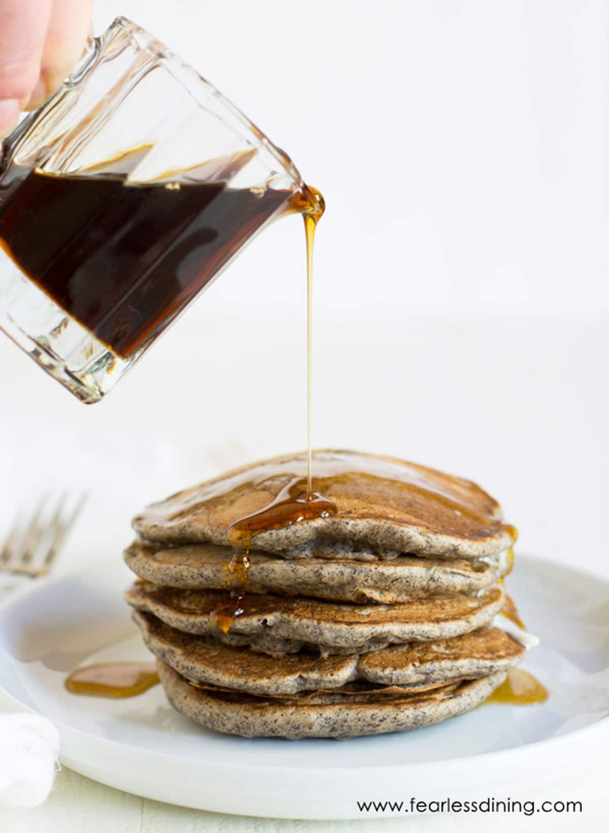 Pouring syrup over a stack of buckwheat pancakes.