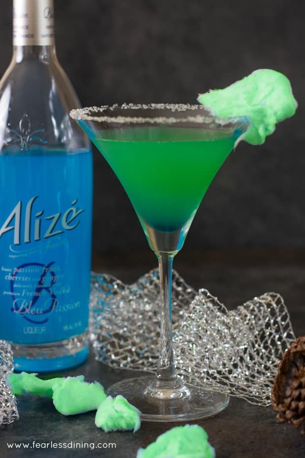 A grinch cocktail next to a bottle of blue Alize.