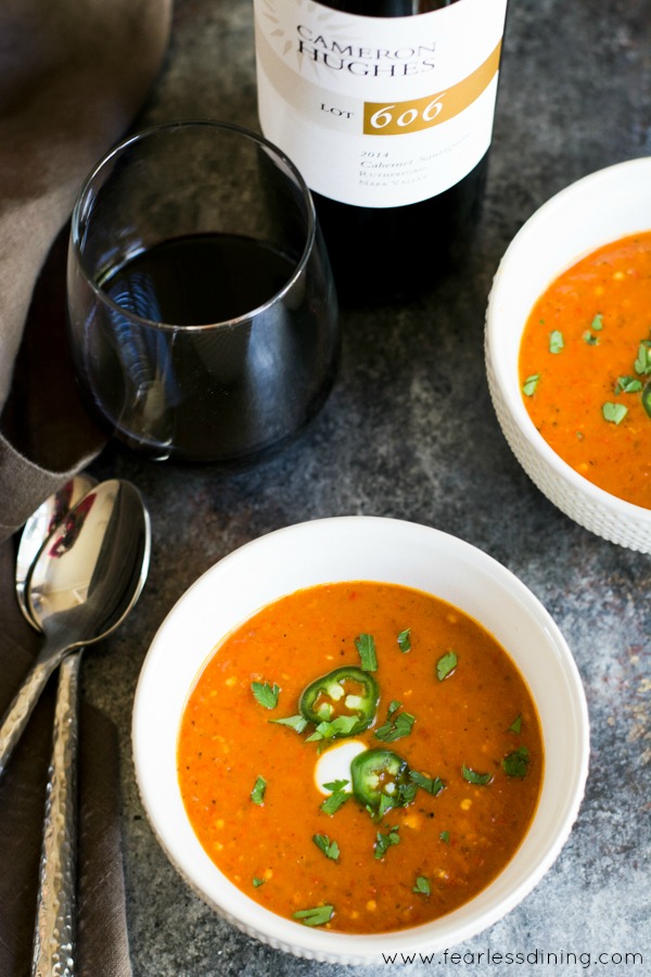 Top view of two bowls of red shishito pepper bisque. A glass of red wine is next to the bowls