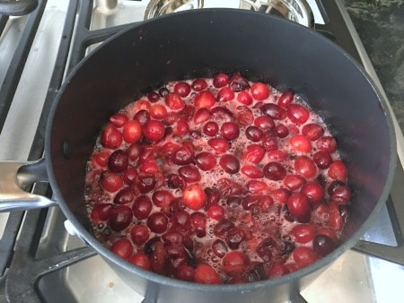 Cooking cranberries in a small pot on the stove.