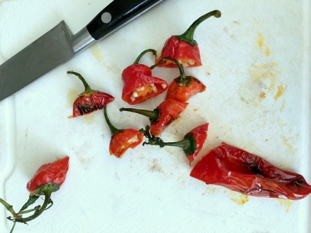 Red blistered shishito peppers on a cutting board. A few stems are next to the chopped pepper