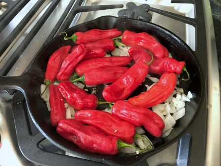 Red shishito peppers cooking in a cast iron skillet.