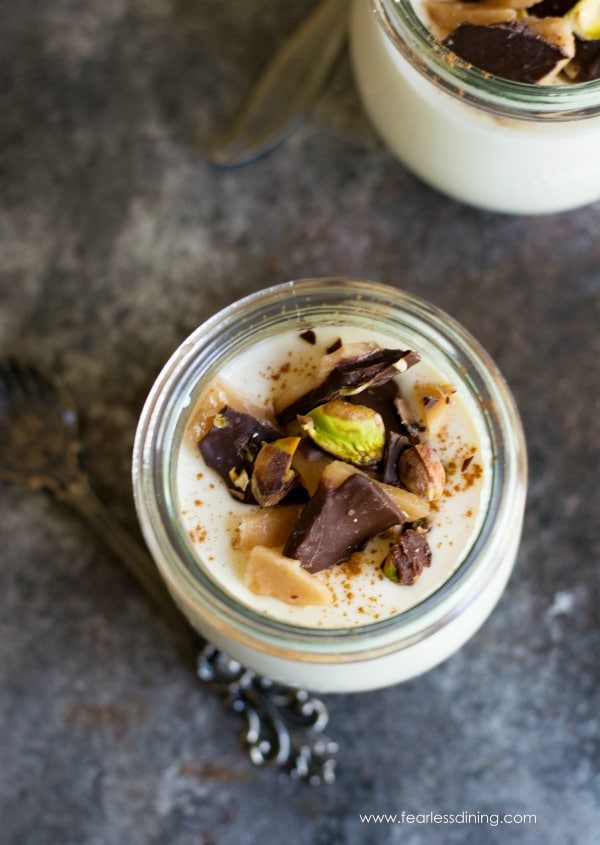 Top view of a glass with eggnog panna cotta. Pieces of toffee and pistachios top this dessert
