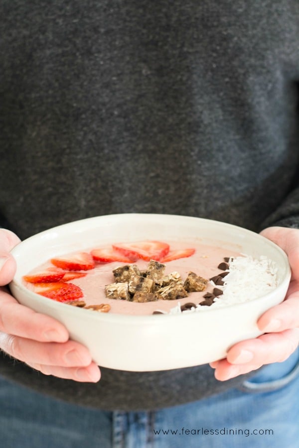 Hands holding a strawberry smoothie bowl.