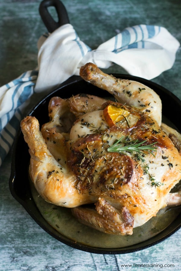 a roasted chicken in a cast iron skillet. Oranges and herbs are stuffed under the skin.