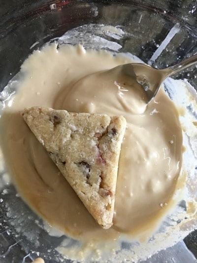 A scone is being dipped into the maple glaze.