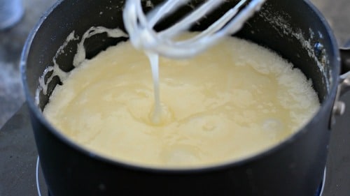 A whisk drizzling some hot toffee back into a sauce pan.