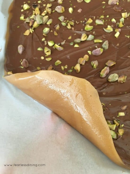Warm pistachio covered chocolate toffee being lifted slightly so you can see the underside