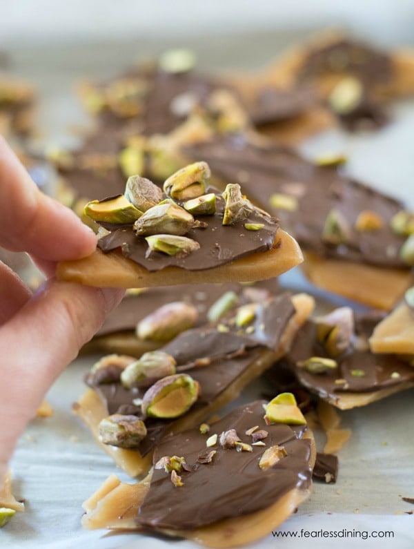 Homemade toffee with chocolate and pistachios. A hand is holding up a piece.