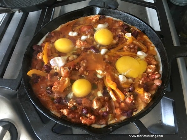 Adding eggs to the cooking shakshuka.