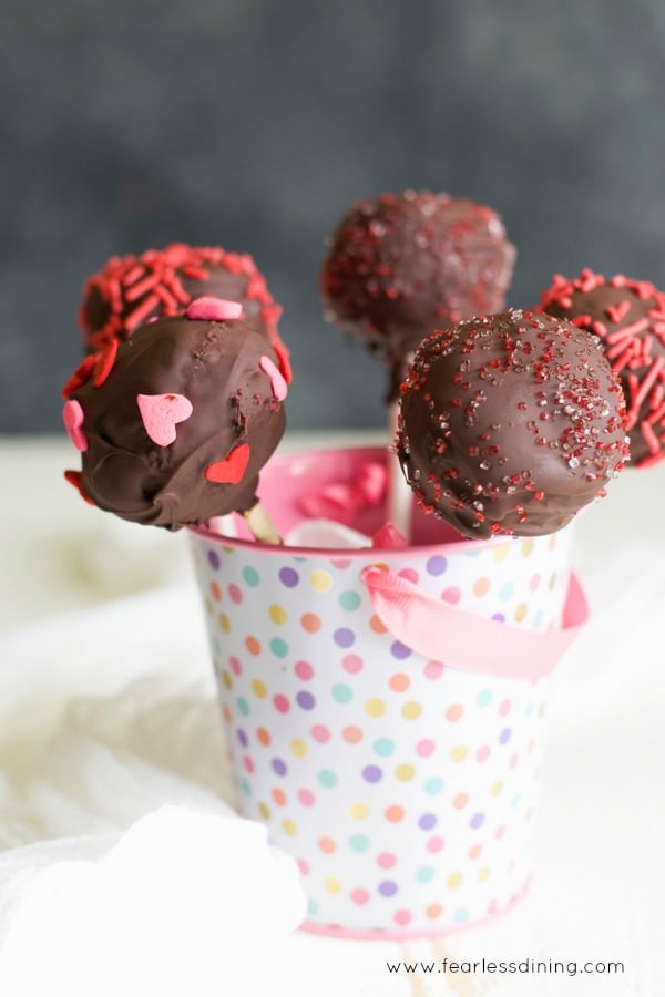 Chocolate cake pops in a rainbow polka dot little bucket. The cake pops are decorated with Valentine's Day sprinkles.