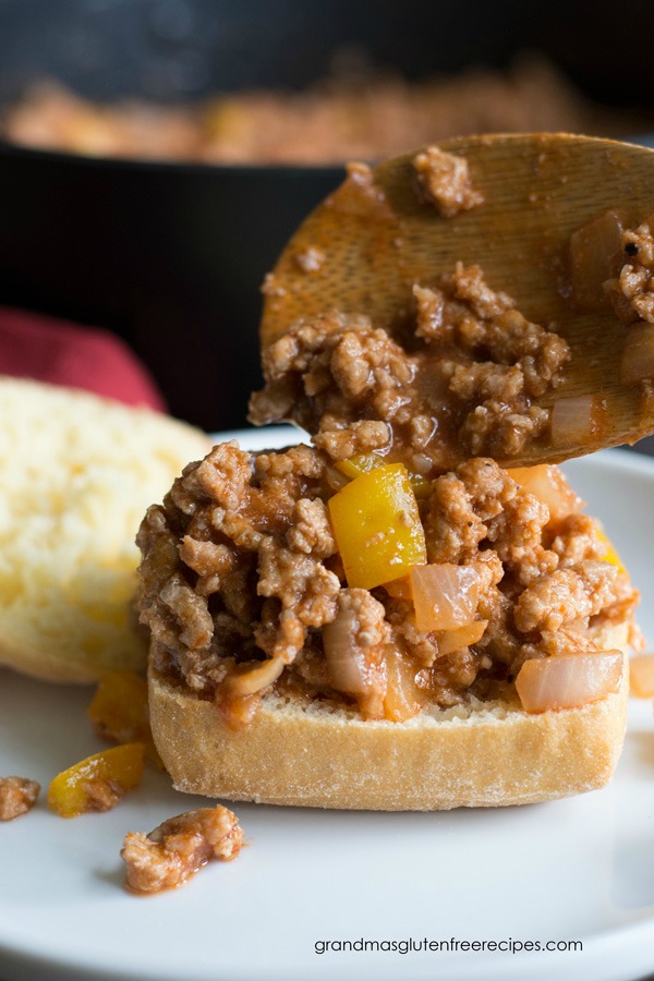 A wooden spoon putting sloppy joe meat onto a gluten free bun.