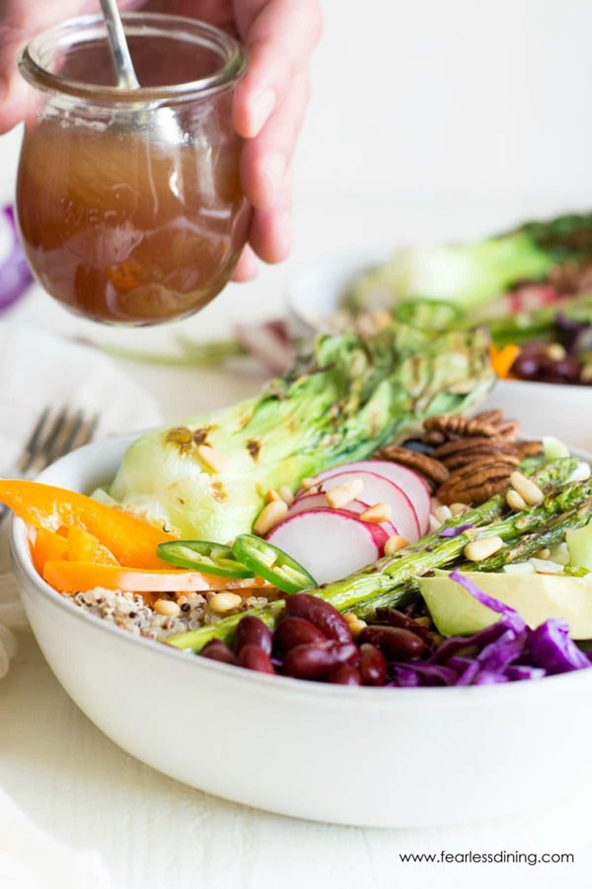 Holding a bottle of dressing over a buddha bowl.