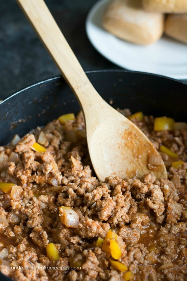 A pot filled with sloppy joe meat, onion, and pepper. A wooden spoon is sticking out of the pot. 