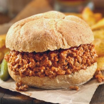 A sloppy joe on a gluten free bun on a platter with fries.