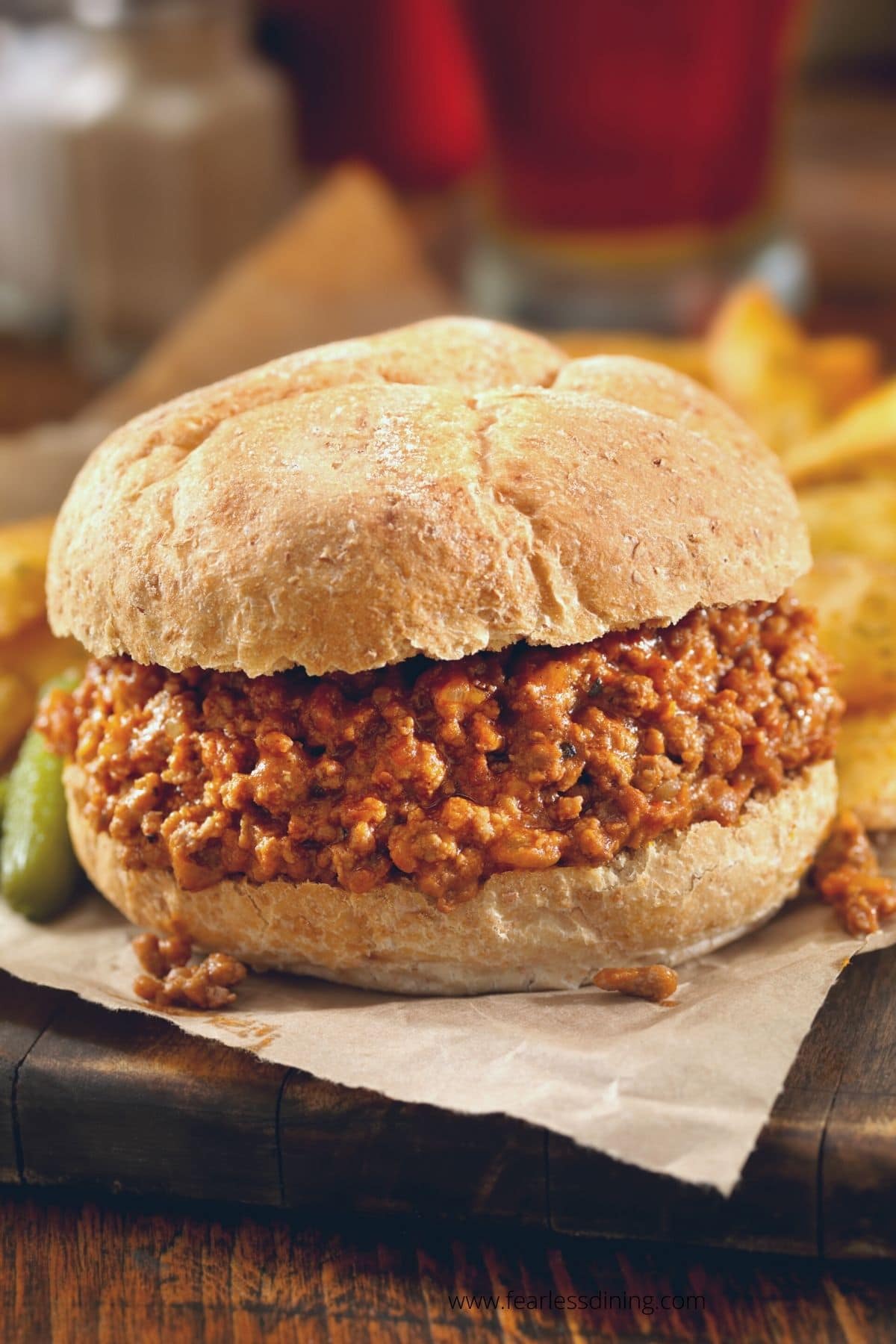 A sloppy joe on a gluten free bun on a platter with fries.