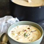 A bowl filled with gluten free fish chowder. It is next to the pot of chowder.