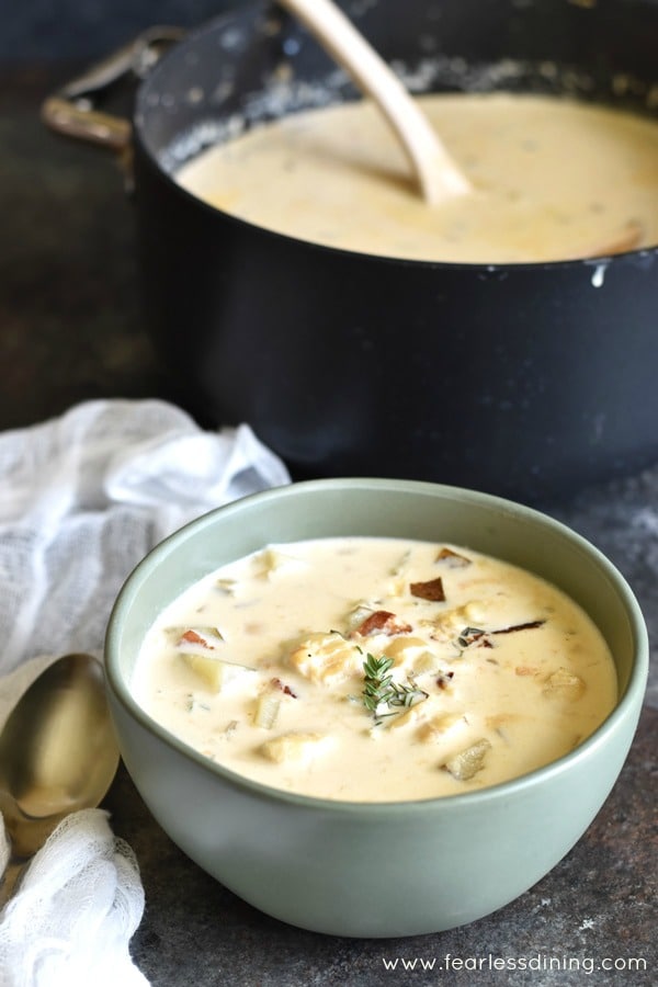 A bowl filled with gluten free fish chowder. It is next to the pot of chowder.