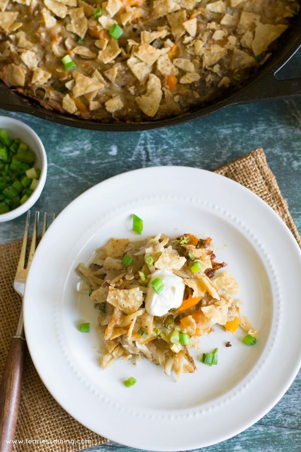 Top view of a plate with a serving of funeral potatoes. The plate is next to the cast iron skillet full of the potatoes.