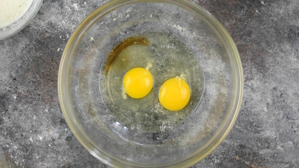 Two raw eggs and vanilla in a glass bowl.