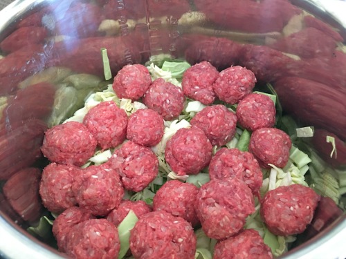 Raw meatballs on top of cabbage in an Instant Pot.