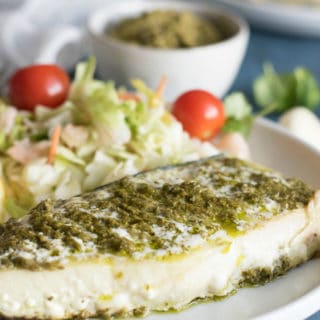 Alaskan halibut topped with pesto on a plate with a side salad.