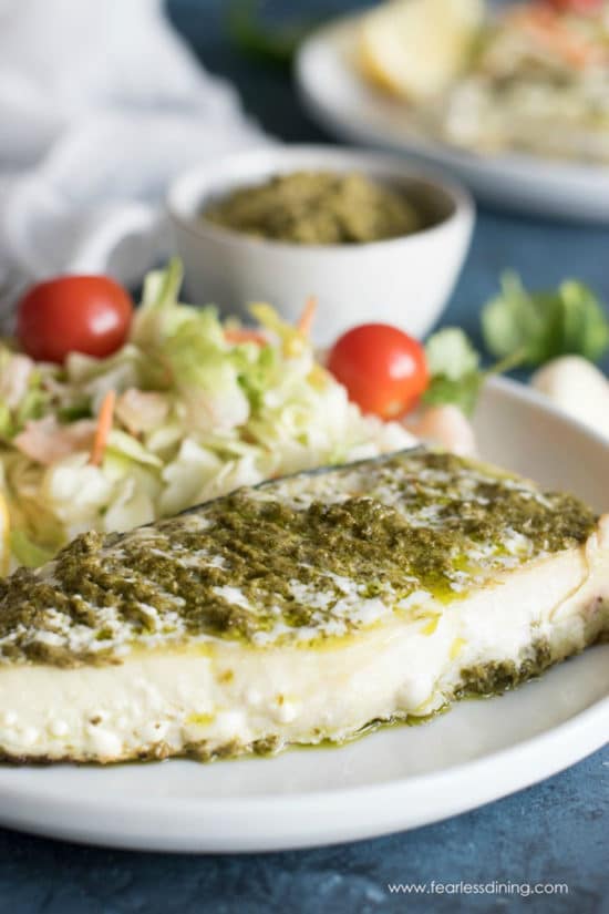 Alaskan halibut topped with pesto on a plate with a side salad.