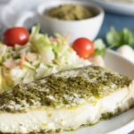 Grilled halibut, topped with pesto sauce on a dinner plate.