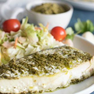 Grilled halibut, topped with pesto sauce on a dinner plate.
