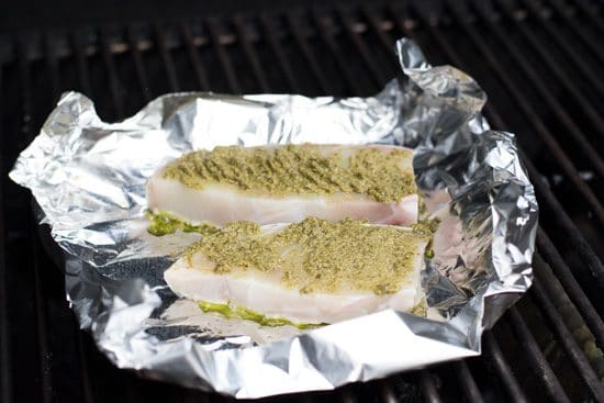 Halibut steaks topped with pesto on top of foil on the grill.