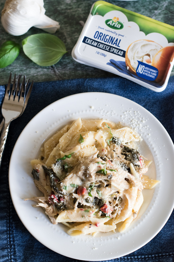 Top view of a plate of penne pasta with cream cheese, garlic clove and basil in the background.