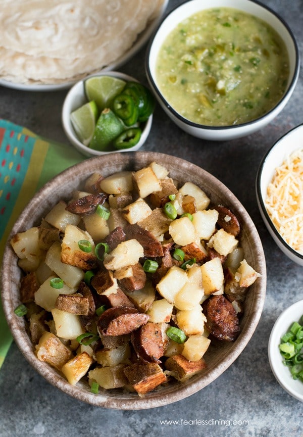 A burrito bar with potatoes and chorizo, salsa verde, tortillas, limes, cheese and scallions