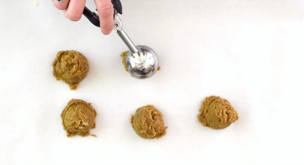 A cookie scoop dropping cookie dough balls onto a baking sheet.