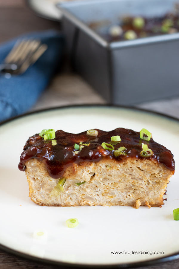 a close up of a slice of turkey meatloaf on a plate with the meatloaf pan in the background