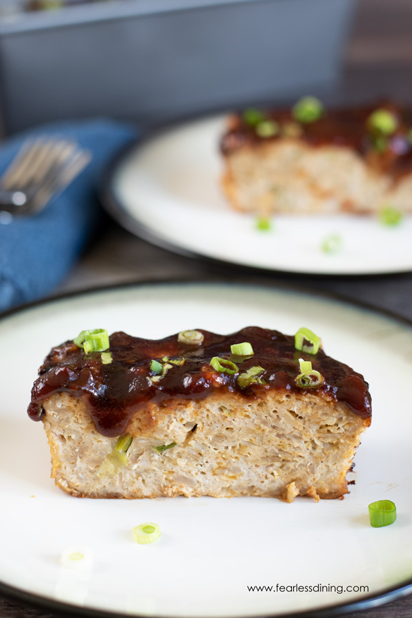 two plates with slices of turkey oat meatloaf with barbecue sauce and chopped scallions on top.