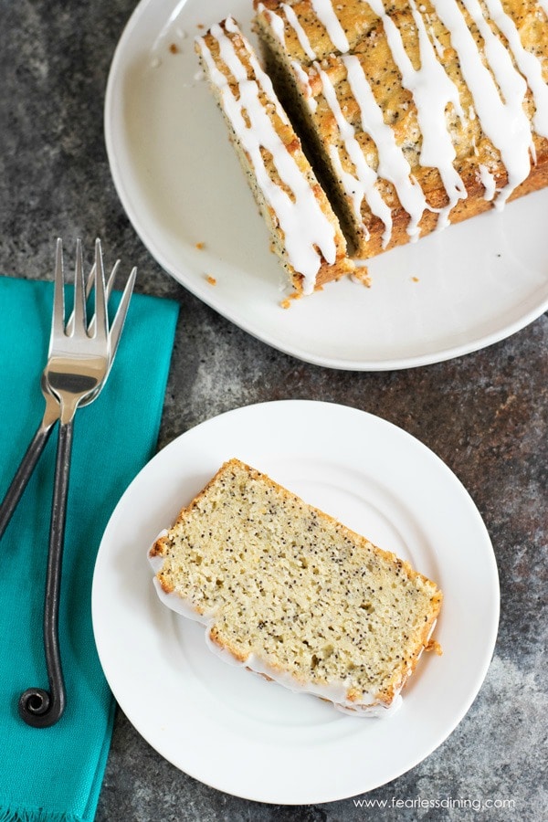 Top view of a slice of lemon poppy seed cake on a plate. The whole lemon loaf is next to the plate.