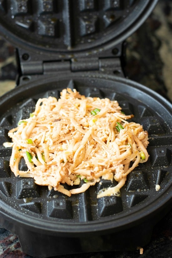 Raw shredded potato and cheese on a waffle maker.