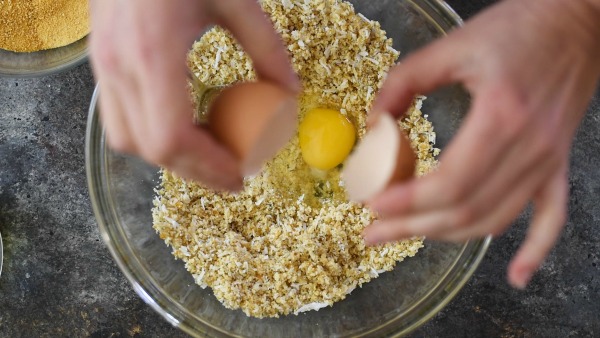 Breaking an egg into the crust ingredients.