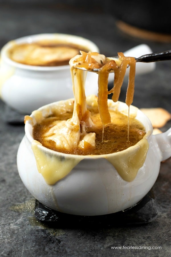A spoon with French onion soup and melted cheese dripping down into the bowl.