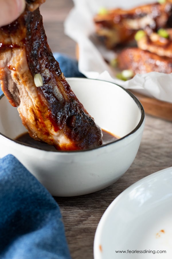 a hand dipping a grilled rib into BBQ sauce.