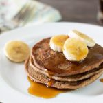 a stack of cassava pancakes with sliced bananas and syrup.